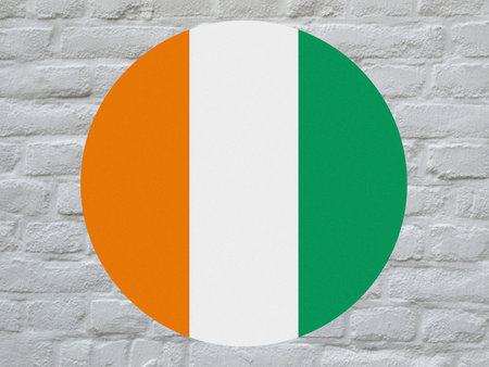 round Ivorian national flag of Cote Ivoire, Africa over white bricks wallの写真素材