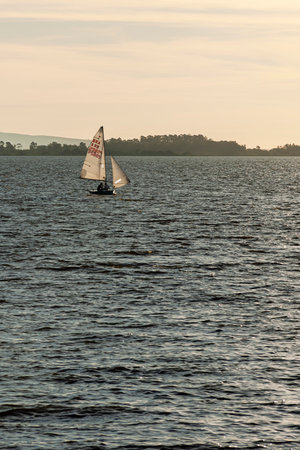 Small boat with two crew members navigating on a calm river in the late afternoon