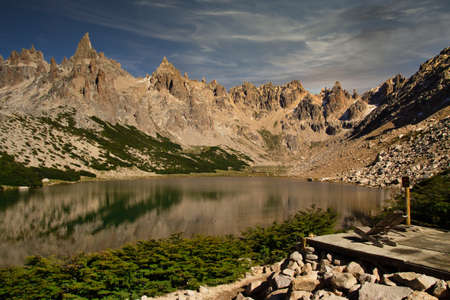 Fantastic cloudy landscape of high and rocky mountains next to its small lake and traveler's refuge.の写真素材