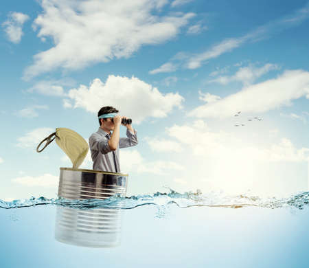young businessman in a can in the ocean scanning the horizon with binocularsの写真素材