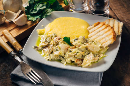 Codfish with polenta and bruschetta served on white plate
