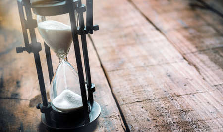 closeup of an hourglass on wooden background in backlight