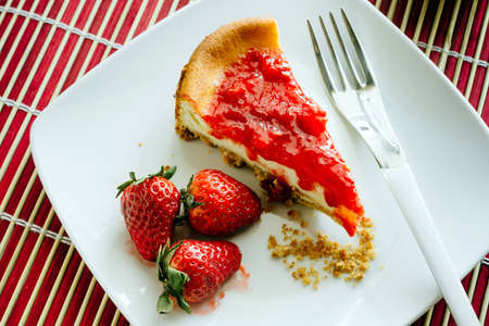 A slice of cheesecake with strawberry jelly on white plate.