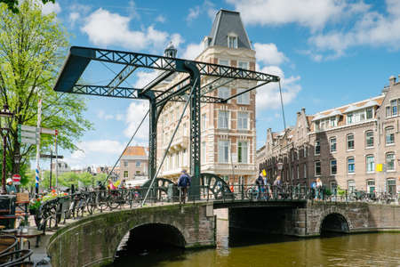 Amsterdam, Netherlands - May 13, 2019: metal drawbridge with people passing by and bicycles resting on the railingのeditorial素材