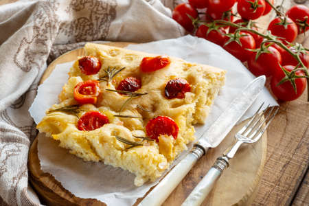 Piece of savory focaccia with olive oil, rosemary and cherry tomatoes on the table