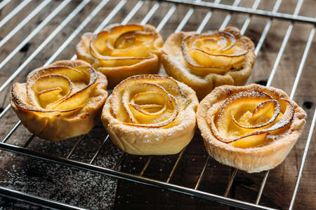 Pastries with custard decorated with apple slices in the shape of a rose on wooden boardsの写真素材
