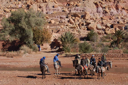 Local man and tourists walks by the bed of river near one of the most extraordinary Kasbahs in Moroccoのeditorial素材