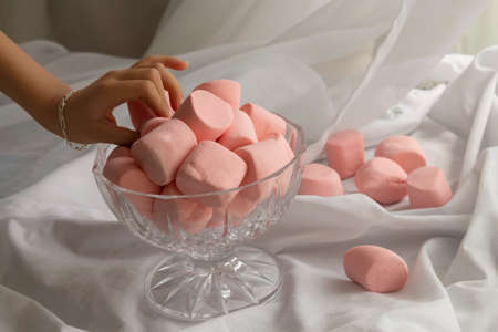 Glass candy with pink marshmallows and a hand taking them