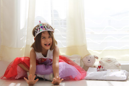 girl playing in front of window with princess crown and stuffed toysの写真素材