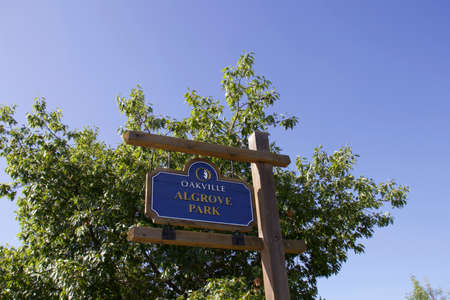 Oakville, Ontario / Canada - September 11, 2020: Algrove Park wooden blue and brown sign at the entrance on White Oaks Blvd. Green tree and blue sky in the background.のeditorial素材