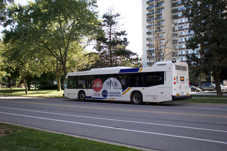 Oakville, Ontario / Canada - September 11, 2020: Oakville transit white bus with big advertising on the side, route 5, on White Oaks Blvd in front of Marlborough Court buildings.のeditorial素材