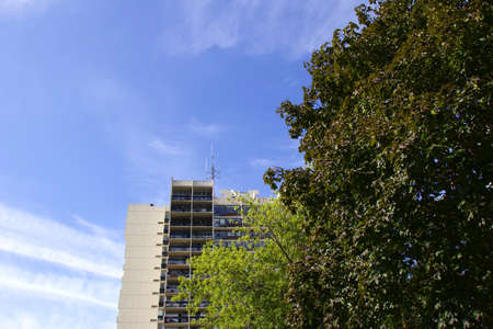 Gray low income building with blue sky background and green trees in foreground. Antennae on the...