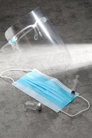 Medical mask, syringe and ampoule on gray background.