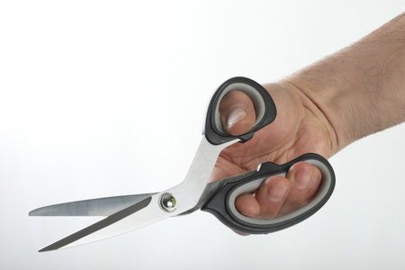 Man's hand holding a pair of black scissors on a white backgroundの写真素材
