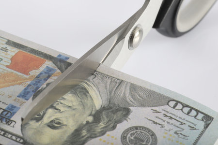Scissors cutting a 100 dollar bill on white background, close upの写真素材