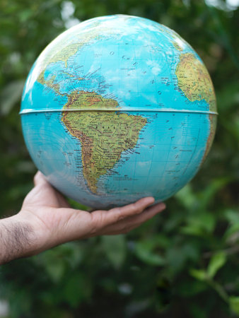Hand holding a globe against the background of greenery. Close-up.の写真素材