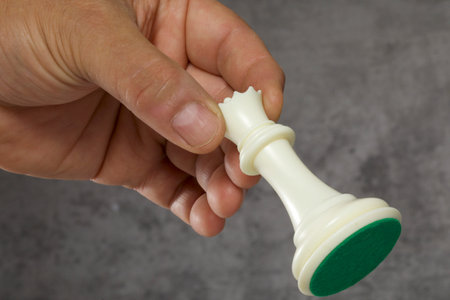Hand holding a white chess piece on a gray background with copy space