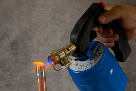 Hand holding a gas burner with a blue flame on a gray background