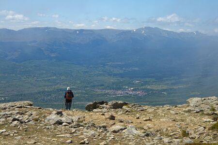 Hiker observing a village from a mountain top with a mountainous landscape in the background.の写真素材