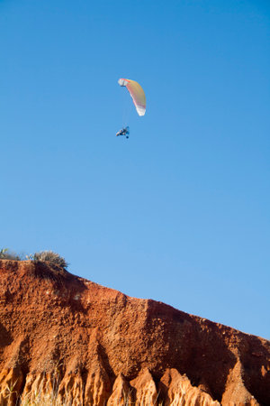 Paraglider with motor over a cliff with blue sky in the background, The technical definition is: ultralight flexible glider. Falesia beach in Algarve, Portugal.の写真素材