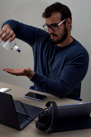 Young caucasian man with glasses and a blue sweater applying hand sanitizer before starting his...