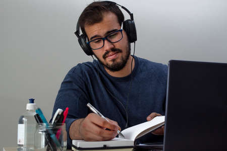 Caucasian young man with glasses working from home on his laptop wearing a blue sweater while...