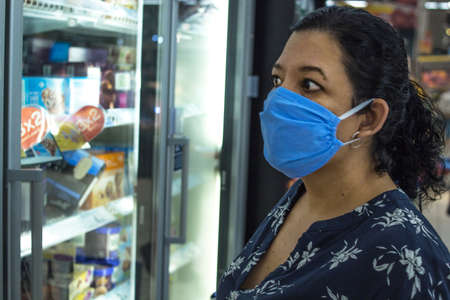 June 10th, 2020. Madrid Spain. Caucasian woman doing shopping in a super market in a blue dress following hygiene rules with a medical mask to protect herself from viruses.のeditorial素材