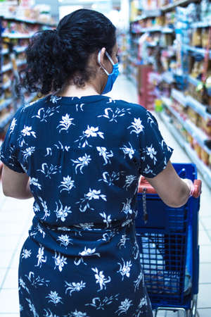 June 10th, 2020. Madrid Spain. Caucasian woman doing shopping in a super market in a blue dress following hygiene rules with a medical mask to protect herself from viruses.のeditorial素材