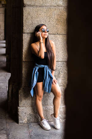 Selective focus of young hispanic woman strolling around a plaza in the city while using her smartphoneの写真素材