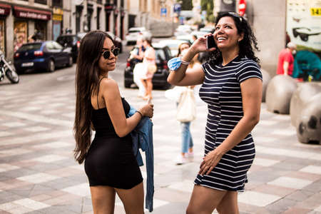 Selective focus of young women walking through the city on a sunny summer day using their mobile devicesの写真素材