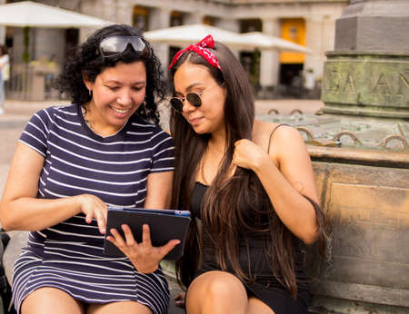 Selective focus of young women walking around a square in the city while using their electronic devicesの写真素材