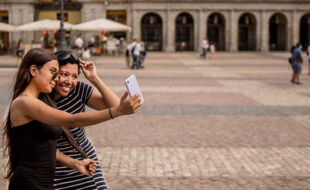 Selective focus of young women walking around a square in the city while using their electronic devicesの写真素材