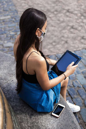 Selective focus of young hispanic woman strolling around a square in the city while using her electronic devices, her smartphone and tabletの写真素材