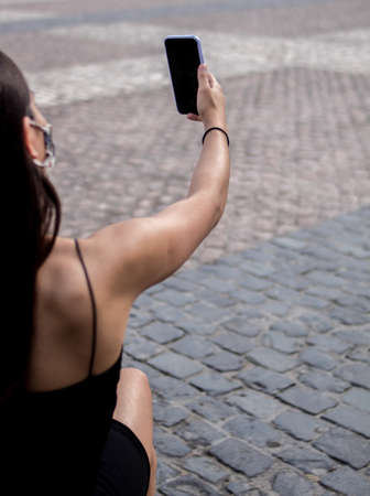Selective focus of young hispanic woman wearing a medical mask while taking selfies with her smartphoneの写真素材