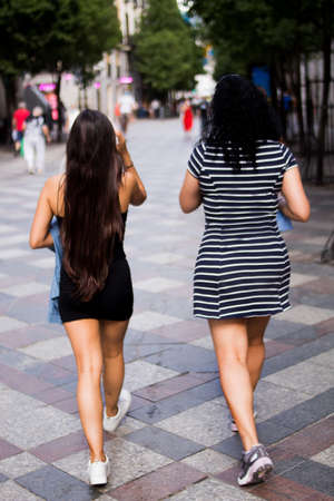 Selective focus of young women walking through the city on a sunny summer day using their mobile devicesの写真素材