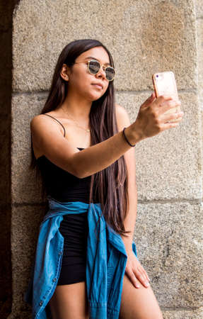 Selective focus of a young Hispanic woman taking selfies while strolling through the cityの写真素材