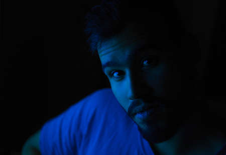 Selective focus portrait of young caucasian man with blue light on his faceの写真素材