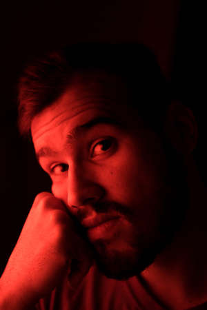 Selective focus portrait of young caucasian man with red light on his faceの写真素材