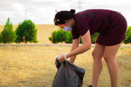 Caucasian woman with gloves and medical mask picking up plastic garbage in the forestの写真素材