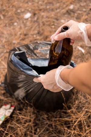 Image of the hands of a Caucasian woman collecting plastic garbage in a meadow