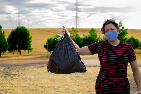 Caucasian woman with gloves and medical mask picking up plastic garbage in the forestの写真素材