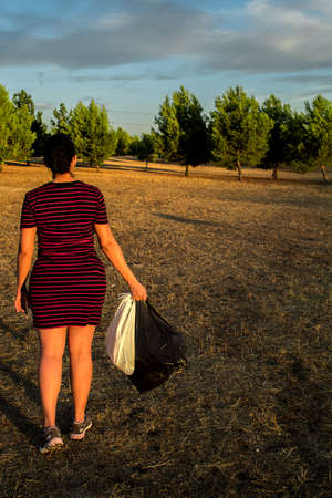 Caucasian woman with gloves and medical mask picking up plastic garbage in the forestの写真素材