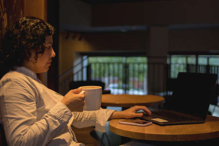 Caucasian woman in a coffee shop working with a laptop while talking on the phone and had a coffee