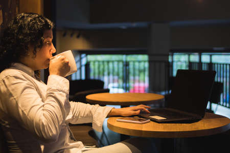 Caucasian woman in a coffee shop working with a laptop while talking on the phone and had a coffeeの写真素材