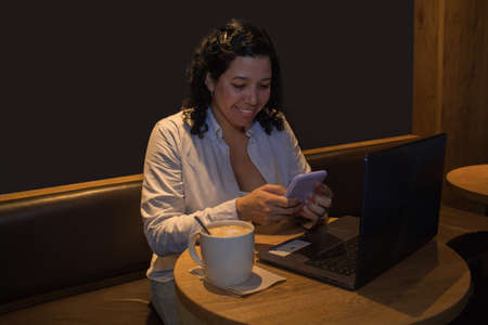 Caucasian woman in a coffee shop working with a laptop while talking on the phone and had a coffeeの写真素材