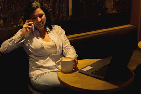 Caucasian woman in a coffee shop working with a laptop while talking on the phone and had a coffee