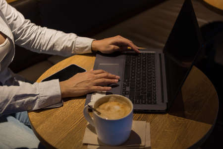 Laptop on a wooden table in a coffee shop with a cup of coffee and a phone by the sidesの写真素材