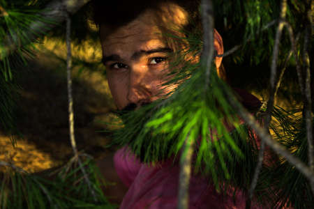 Portrait of caucasian man with beard and black hair in the forest through some branchesの写真素材