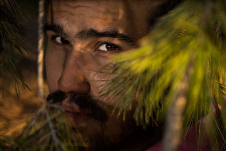 Portrait of caucasian man with beard and black hair in the forest through some branchesの写真素材