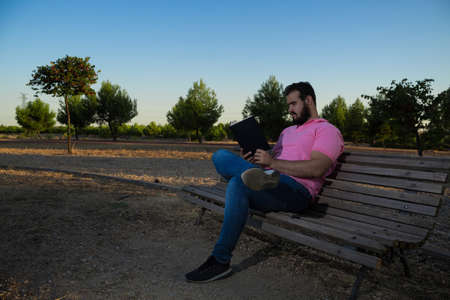 Caucasian man reading a book in the park while wearing a pink shirt and jeansの写真素材